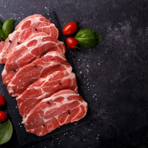 Slices pork loin with herbs salt and pepper black stone background copy space flat lay
